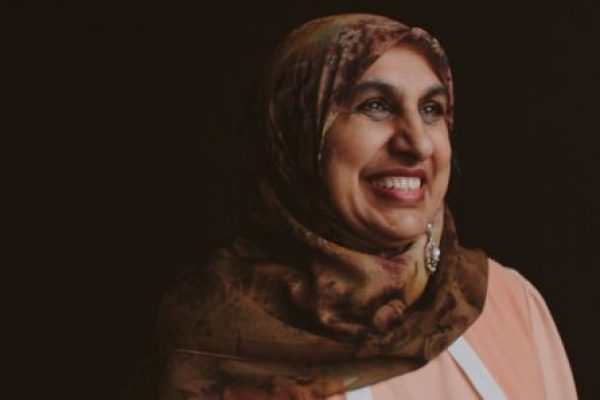 Portrait of Anjum Rahman smiling with black background