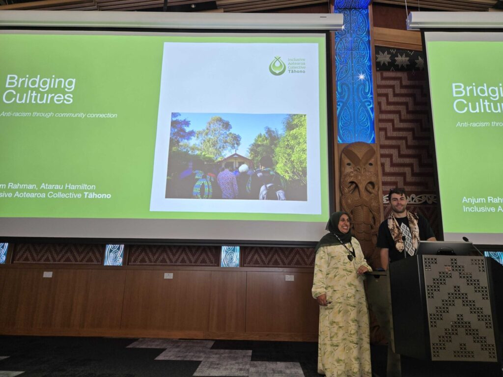 Anjum and Atarau posing in front of their presentation slides in event space