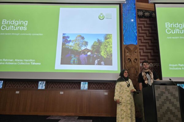 Anjum and Atarau posing in front of their presentation slides in event space